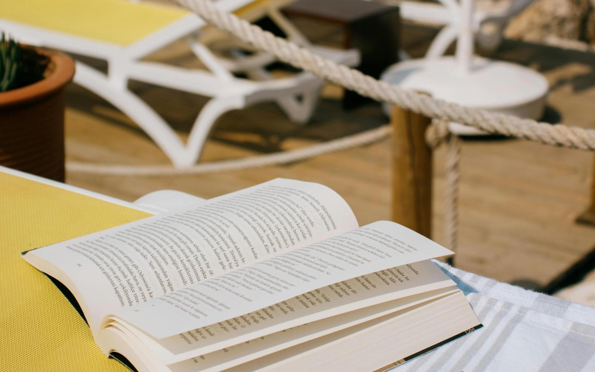 Symbolbild Sonnenbrille, aufgeschlagenes Buch, Badetuch